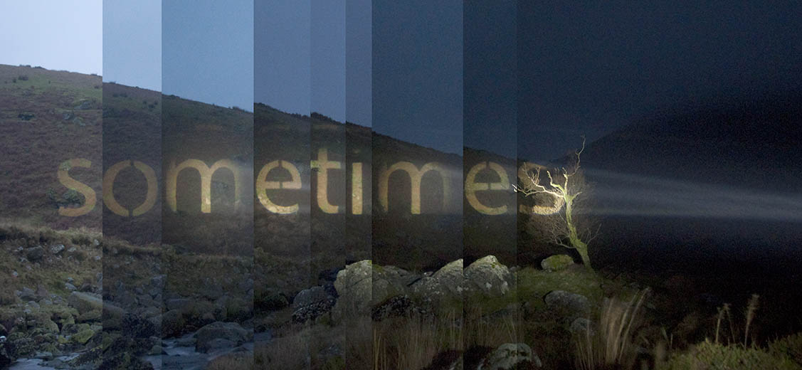Link to a projector project by Michael Cross. Text works made with a powerful projector that projects words onto the landscape. Image shows the word Sometimes projected onto a hillside.